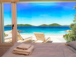 A room with a large window overlooking a beach, two lounge chairs, and a neatly made bed. - Buqez - Villa 27 by Interhome (Pakoštane/Drage)