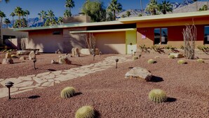 A modern building with a desert garden featuring cacti and rocks, a stone pathway, and a mountain backdrop. - Star of Modernism Week - Three Bedrooms, Pool &Spa in Historic Deepwell Estates (Palm Springs)