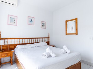 A hotel room with a wooden bed, white linens, a bedside table with a lamp, and three framed pictures on the wall. - Los Pinos 23 Villas by Casasol by Interhome (Nerja)