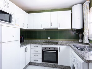 A compact kitchen with white cabinets, a built-in oven, a microwave, a kettle, and a washing machine. - Los Pinos 23 Villas by Casasol by Interhome (Nerja)