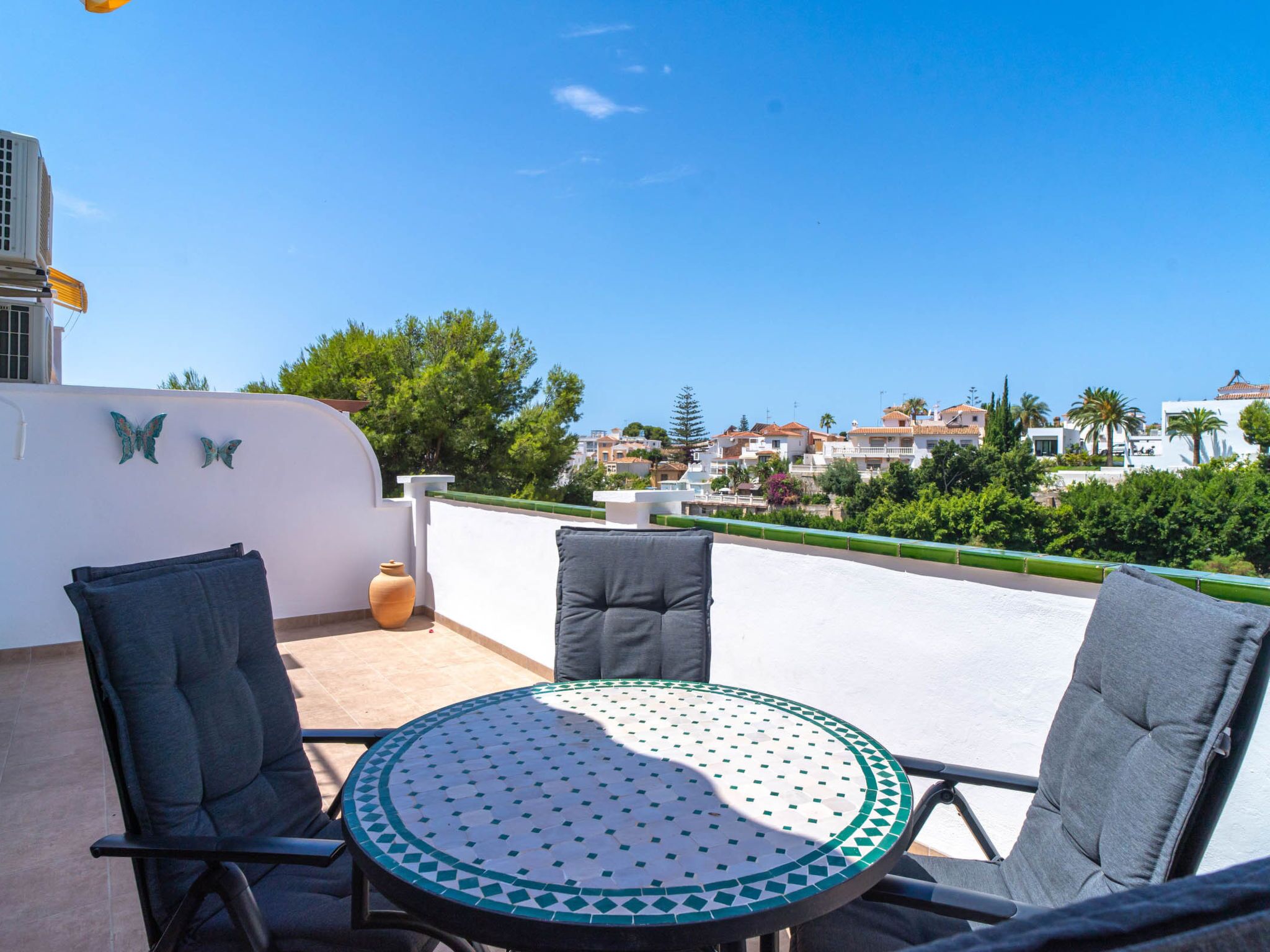 Una terraza con una mesa redonda y dos sillas, con vistas a un pueblo costero con edificios y vegetación.