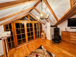 A high-ceilinged attic room with wooden beams, a large window, a fireplace, and a television. - Schönblick - Daniela 7 by Interhome (Rauris)