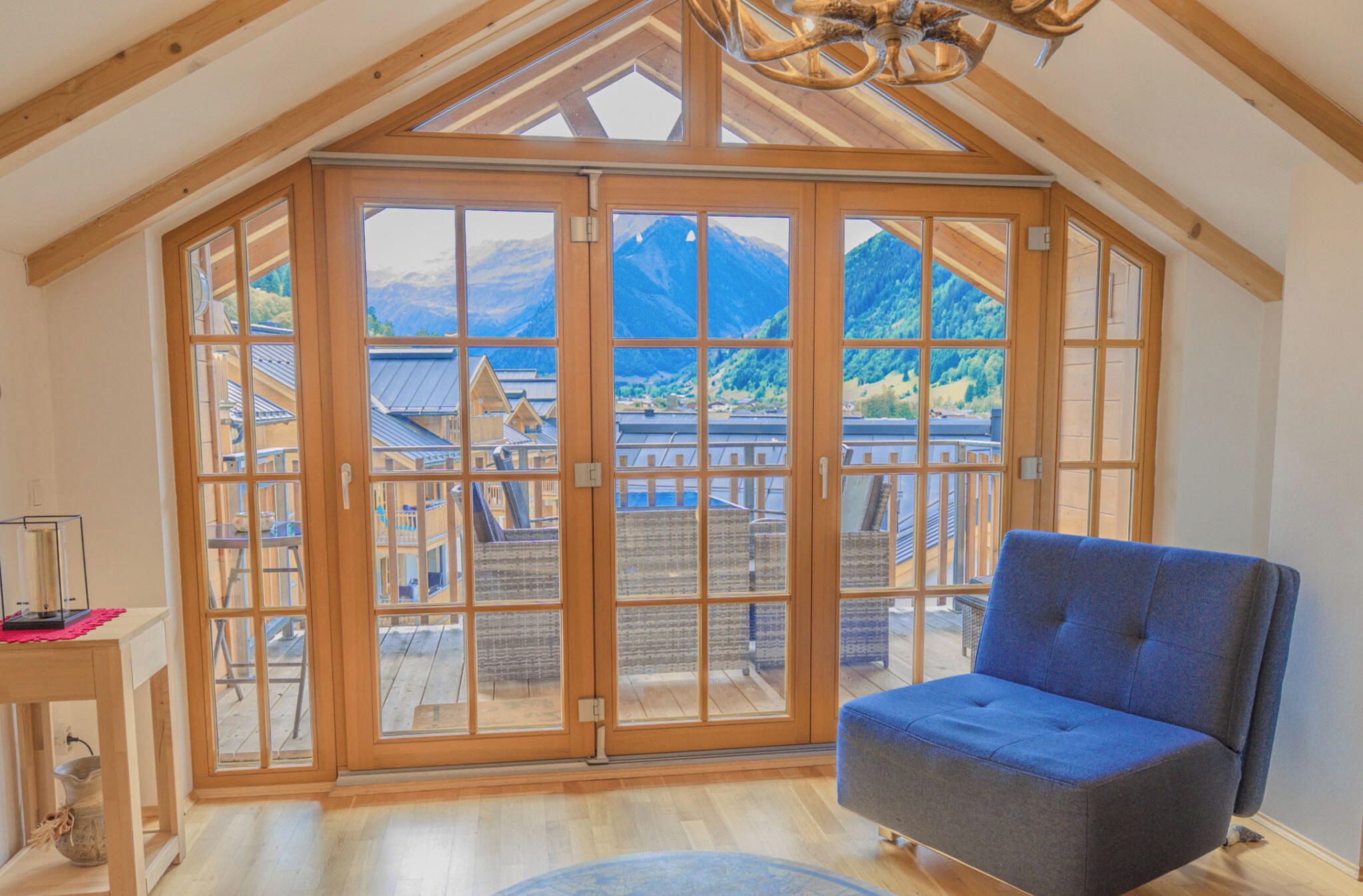 Une pièce dotée d’une grande fenêtre à cadre en bois, d’une chaise bleue et d’un plafond en bois.