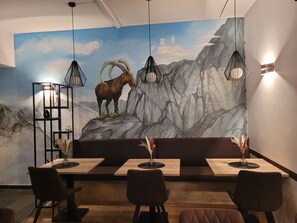 Ein Restaurant mit Wandmalerei einer Berglandschaft, Pendelleuchten und Holztischen.