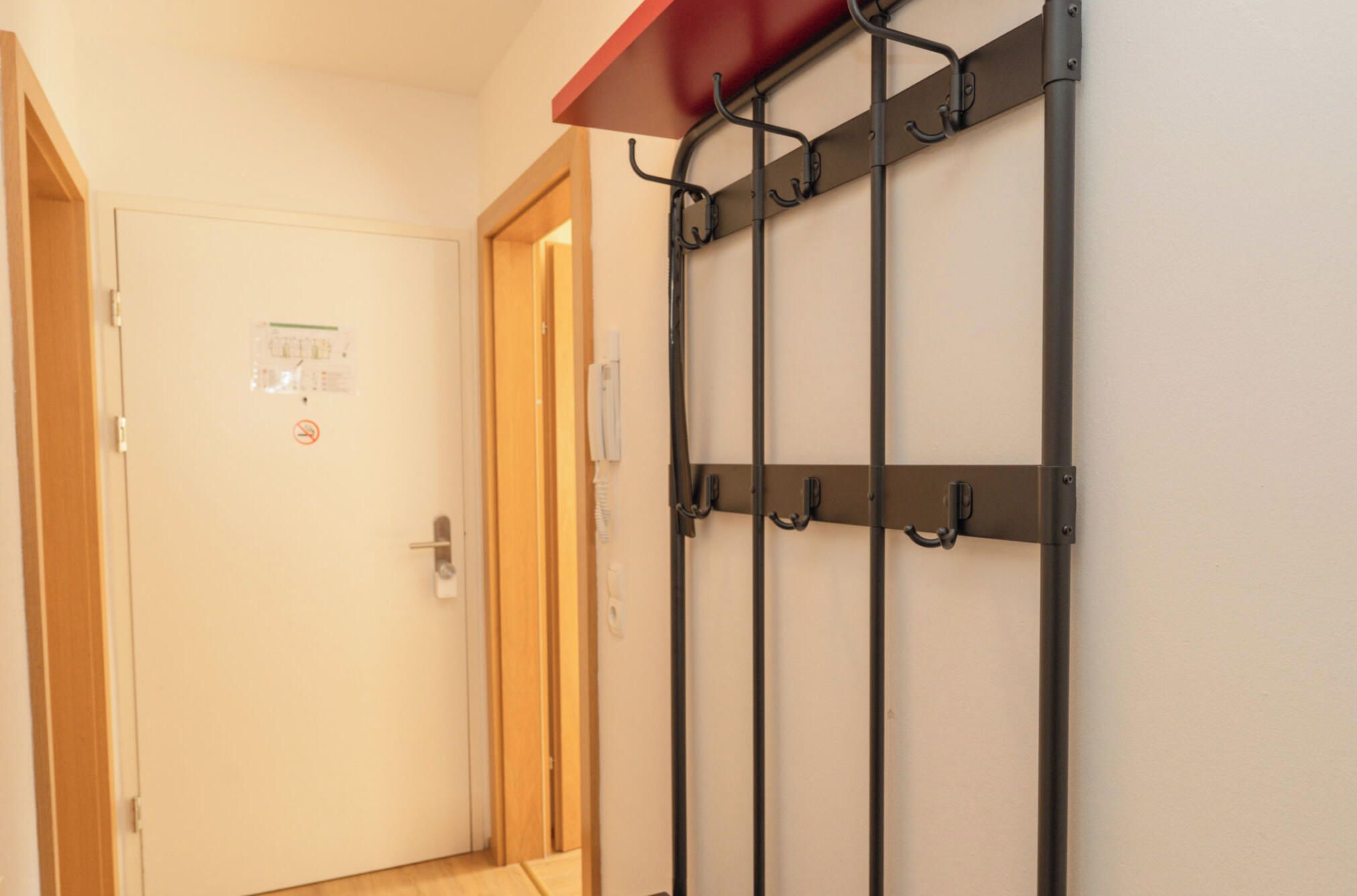 A hallway with a door, a coat rack, and a wall-mounted light switch.