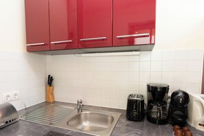 A kitchen with a stainless steel sink, red cabinets, a knife block, a toaster, and a coffee maker. - Schönblick - Daniela1 by Interhome (Rauris)
