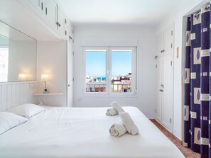 A hotel room with a large bed, two bedside lamps, a window with a view of buildings, and a door with a curtain. - Apartment  by Interhome (Nerja)