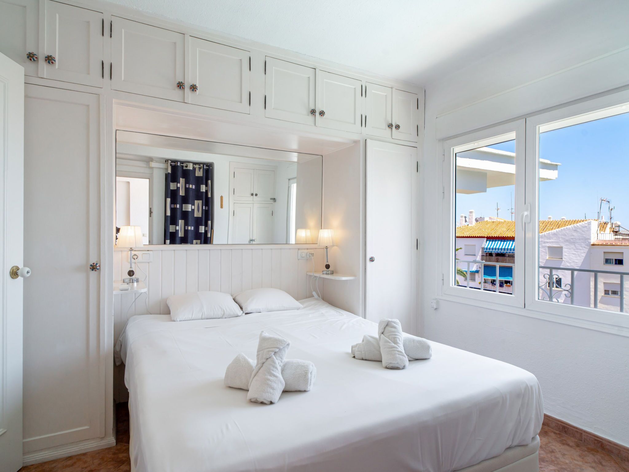 Ein Hotelzimmer mit einem großen Bett, einem Spiegel, einem Fenster mit Ausblick und weißen Schränken.