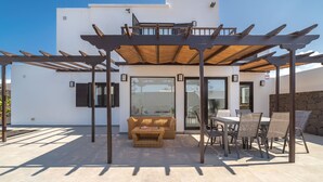 Een overdekt terras met een pergola, een bank en een eettafel met stoelen.