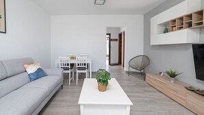 Een moderne woonkamer met een grijze bank, een witte salontafel en een eethoek met een witte tafel en stoelen.