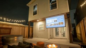 Et hus med et insektnetdækket veranda, bålsted og et fjernsyn der viser en streamingtjeneste.
