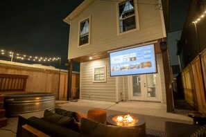 Ein Haus mit einem Moskitonetz-veranda, einem Feuerkorb und einem Fernseher, der einen Streaming-Dienst anzeigt.