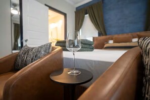 Ein Hotelzimmer mit einem Bett, einem kleinen runden Tisch mit einem Glas Wasser und Ledersesseln.