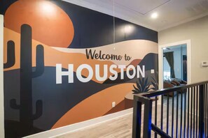 Eine Wand mit einem 'Welcome to Houston'-Mural, eine Treppe und ein Blick in einen Raum mit einem Bett und einem Fenster.