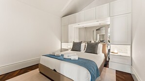 A bedroom with a bed, a nightstand, a mirror, and built-in storage cabinets. - GuestReady - Clérigos Luxury (Porto)