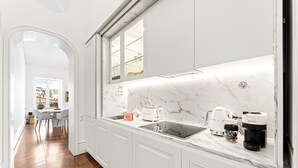 A modern kitchen with white cabinetry, a marble countertop, and a view of the city through a window. - GuestReady - Clérigos Luxury (Porto)