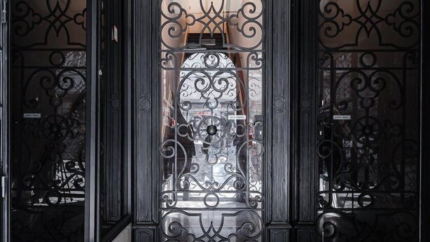 An interior hallway with ornate black metal railings, a marble floor, and a large glass door with intricate designs. - GuestReady - Clérigos Luxury (Porto)