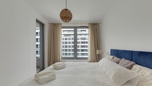 A hotel room with a large bed, a blue headboard, and a view of a building through the window. - Plac Unii by Grand Apartments (Gdynia)