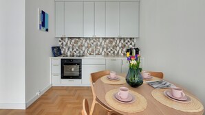 A modern kitchen with white cabinets, a patterned backsplash, and a dining table set with pink cups and a vase of flowers. - Plac Unii by Grand Apartments (Gdynia)