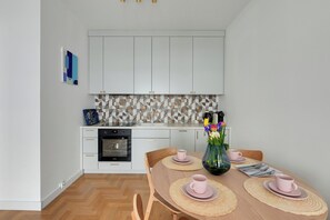 A modern kitchen with white cabinets, a patterned backsplash, and a dining table set with pink cups and a vase of flowers. - Plac Unii by Grand Apartments (Gdynia)