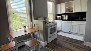A kitchen with a gas stove, oven, white cabinets, and a dining table with benches. - Cozy Private 1BR in the Heart of 5 Points (Denver)