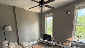 A living room with a sofa, coffee table, TV, and a ceiling fan. - Cozy Private 1BR in the Heart of 5 Points (Denver)