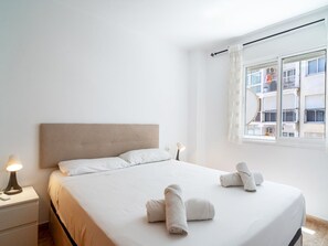 Ein Hotelzimmer mit einem Bett, zwei Nachttischlampen, einem Fenster mit Blick auf ein Gebäude und zwei zusammengerollte Handtücher auf dem Bett.