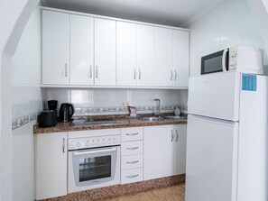 Una cocina compacta con gabinetes blancos, horno empotrado, microondas y encimera de granito.