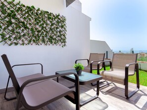 Ein Außenbereich mit Sitzgelegenheit, einem Tisch, Stühlen, einem Blumentopf und einer an der Wand befestigten Pflanzwand.
