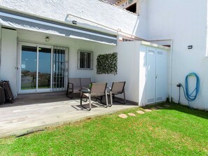 Eine Terrasse mit Tisch und Stühlen, ein überdachter Bereich und ein Rasenstück.