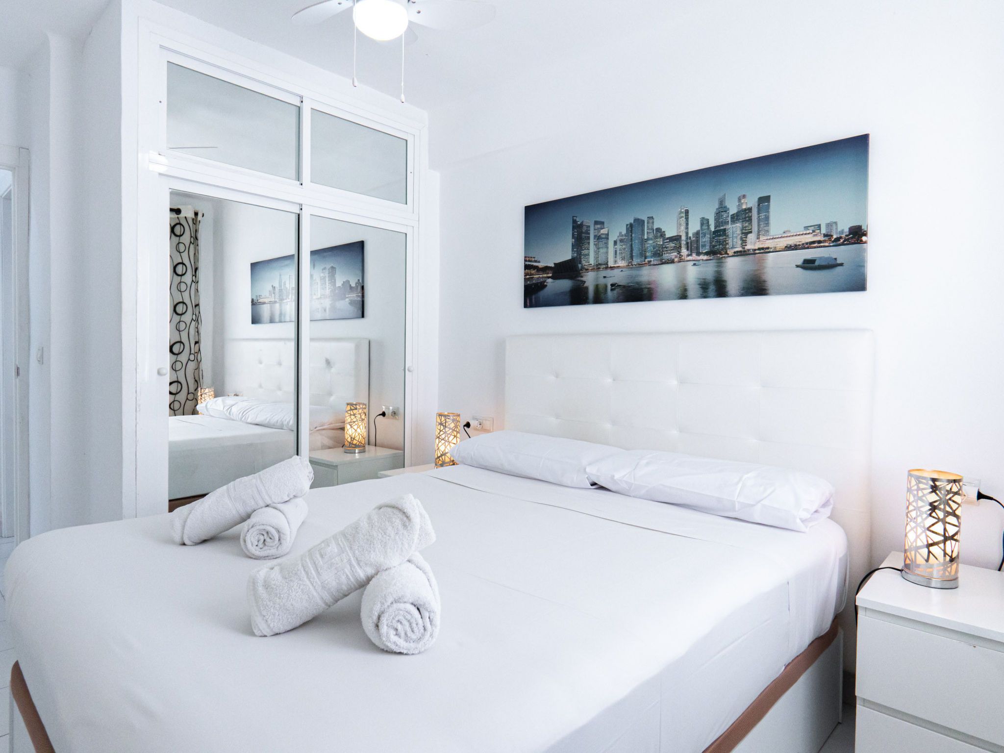 Une chambre d’hôtel avec un grand lit, deux tables de chevet, un tableau représentant un paysage urbain et une vue sur les toits de la ville.