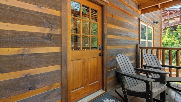 A wooden cabin with a wooden door, two Adirondack chairs, and a porch with a railing. - Sleeps 20 | Private Indoor Pool, Theater, Arcade (Sevierville)