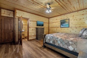 Ein Schlafzimmer mit Holzwänden, einem Bett, einem Schminktisch und einem Deckenventilator.
