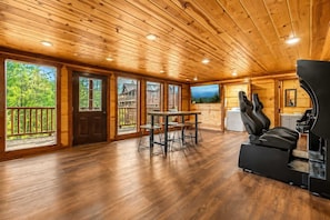 Ein geräumiges Zimmer mit Holzböden, einer Essecke mit Tisch und Stühlen, einem großen, an der Wand befestigten Fernseher und einer Sitzecke mit Sofa und Massagesessel.