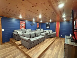 A home theater room with a sectional sofa, wooden flooring, and blue walls. - 6-Bedroom Cabin with Indoor Pool, Home Theater & Hot Tub, Sleeps 20+ (Sevierville)