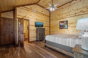 A wooden cabin interior with a bed, a dresser, a television, and a ceiling fan. - 6-Bedroom Cabin with Indoor Pool, Home Theater & Hot Tub, Sleeps 20+ (Sevierville)