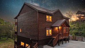 Eine zweistöckige Holzhütte mit Balkon, Treppe und einer Terrassenfläche.