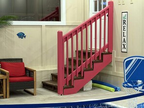 Eine Treppe mit roten Geländern führt zu einer Zwischenebene, dort steht ein Korbstuhl mit rotem Kissen, und ein an der Wand befestigtes Schild mit der Aufschrift 'RELAX'.