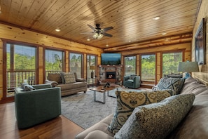 A spacious living room with wooden ceilings, a fireplace, and large windows.