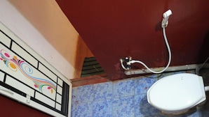 A bathroom with a tiled floor, a white toilet, a blue basin, and a wall-mounted electrical outlet. - Sakleshpur Calm Stay (Alur)