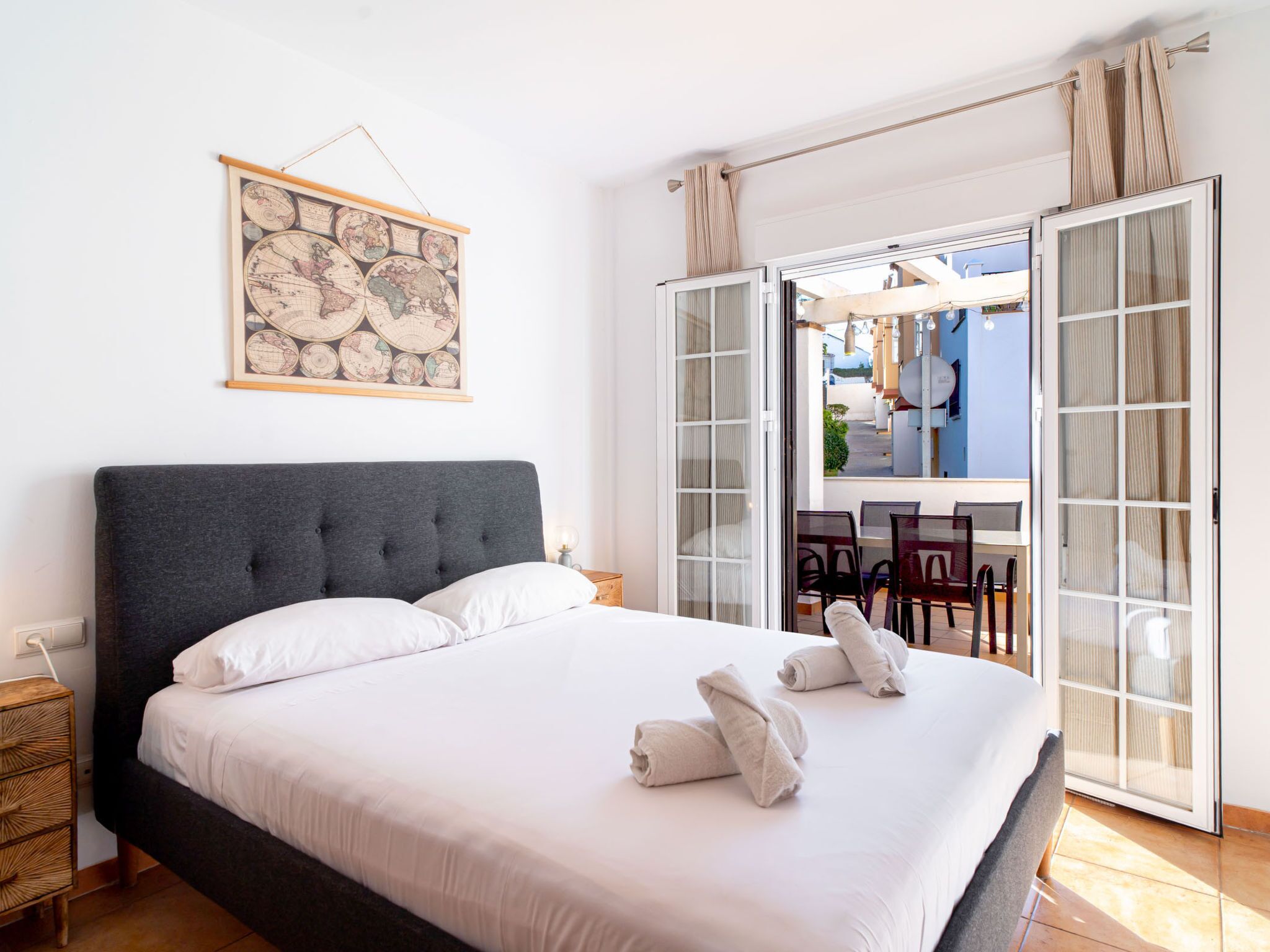 Une chambre d’hôtel avec un grand lit, une œuvre d’art représentant une carte, une vue sur l’extérieur et un balcon avec des chaises.