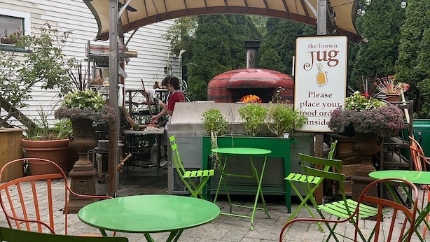 En uteservering med en tegelugn, gröna och orange stolar samt en skylt med namnet på stället, ”The Brown Jug”.