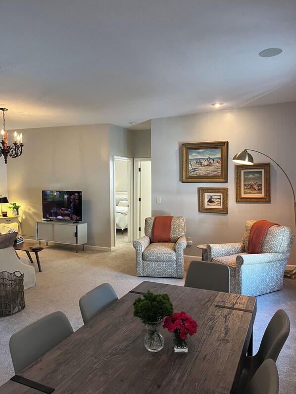 Una sala de estar moderna con una mesa de comedor, dos sillones estampados, un televisor y cuadros en la pared.