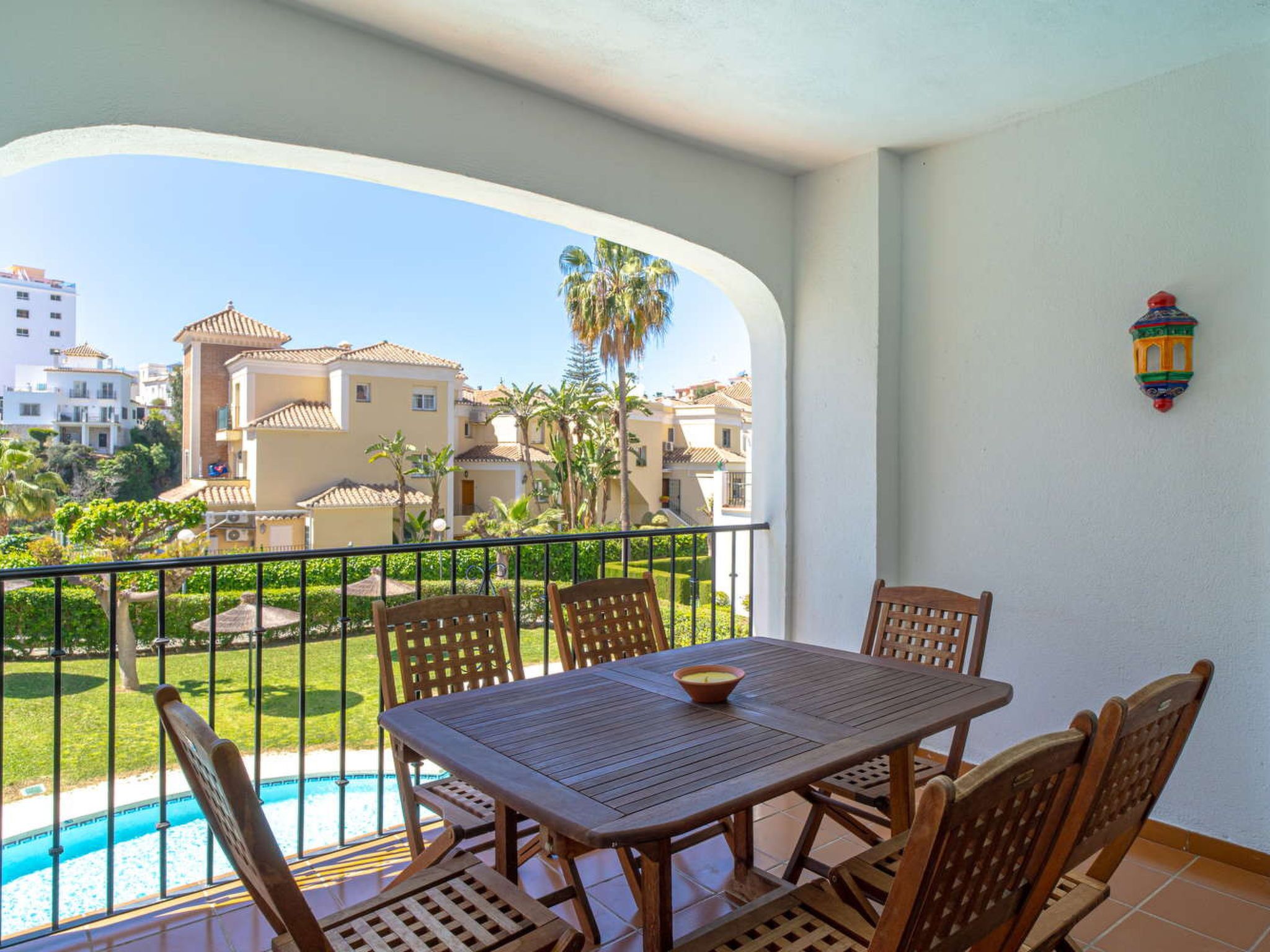 A balcony with a table and chairs, a pool, and a view of buildings and palm trees.