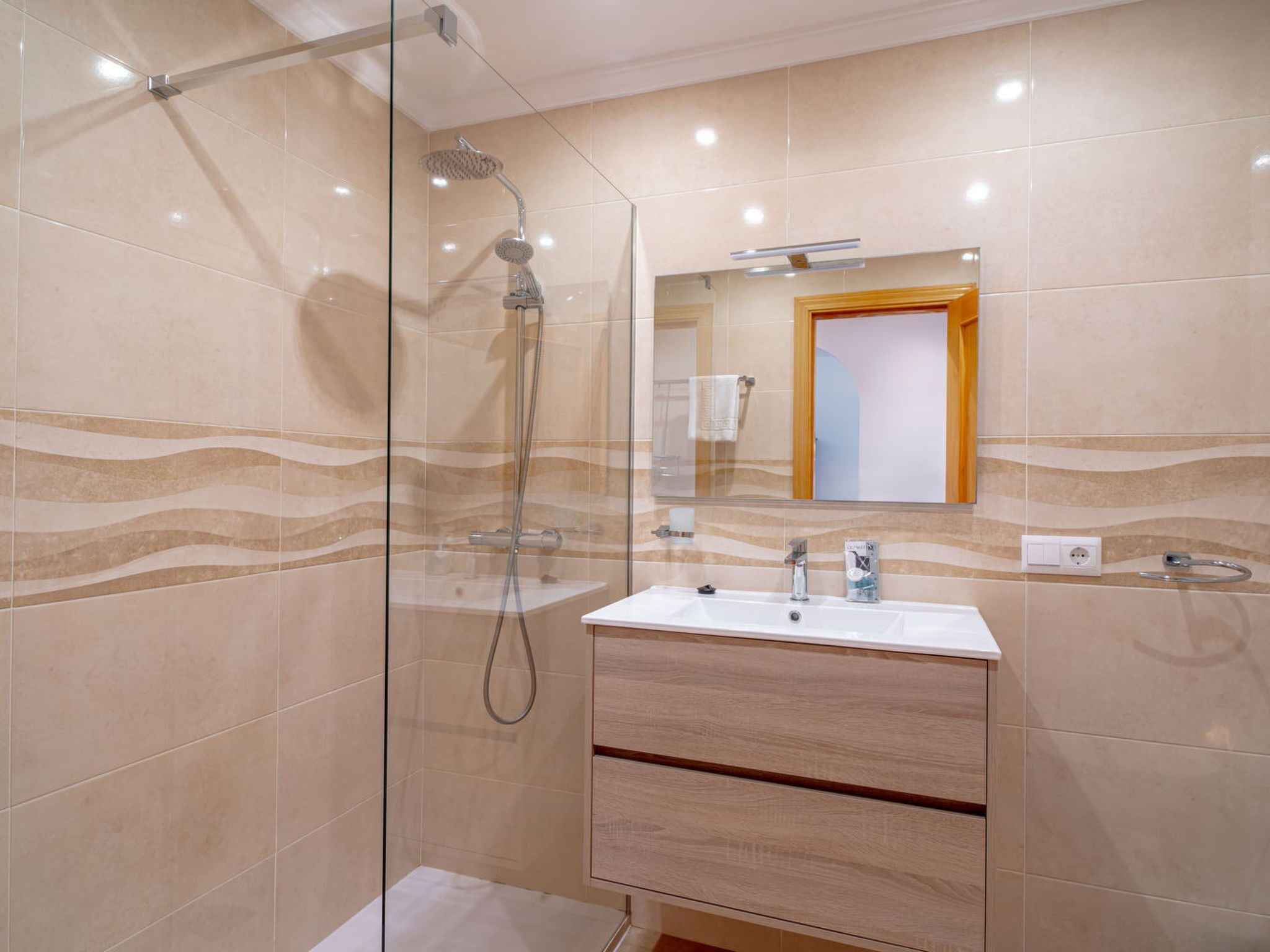 Un bagno moderno con doccia vetrata, lavabo con mobile in legno e specchio sopra il mobile.