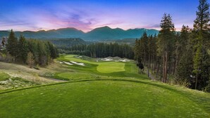 Ein Golfplatz mit einem Haus im Vordergrund und Bergen im Hintergrund.