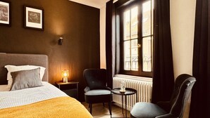 Ein Hotelzimmer mit einem Bett, zwei Stühlen, einem kleinen Tisch, einem Fenster mit Vorhängen und einer Heizung.