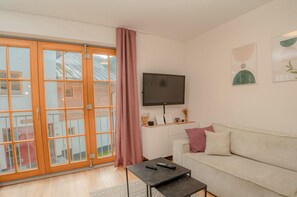 Un saló amb un sofà, una taula de centre, una televisió penjada a la paret i una porta corredissa de vidre que dona a una zona exterior.