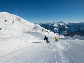 Pista d'esquí nevada amb esquiadors, un telefèric i una muntanya al fons.