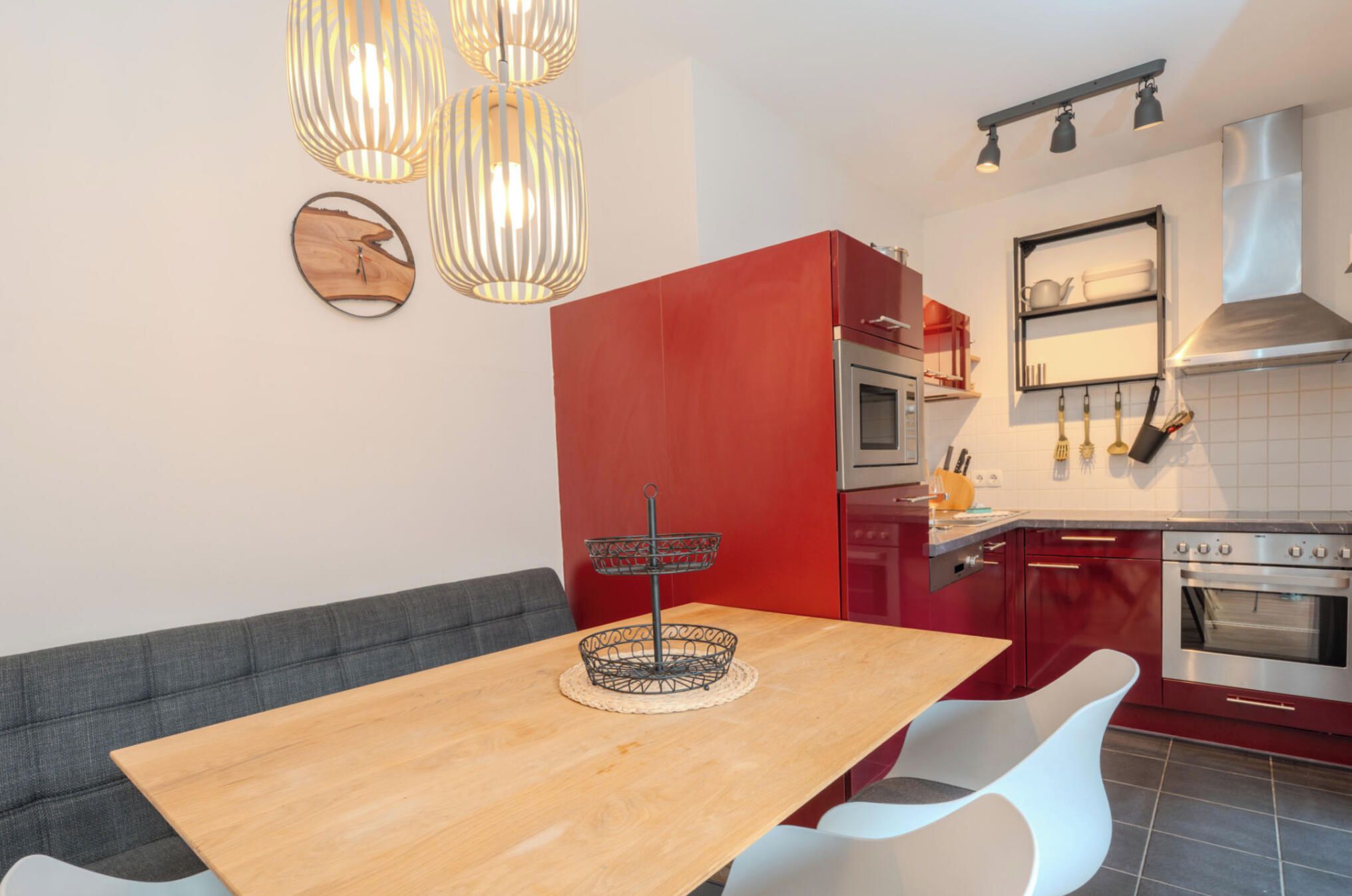 A modern kitchen with a wooden dining table, red cabinetry, and stainless steel appliances.
